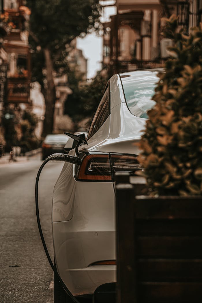 gallery-1 White electric car charging on an urban city street, emphasizing eco-friendly transportation.